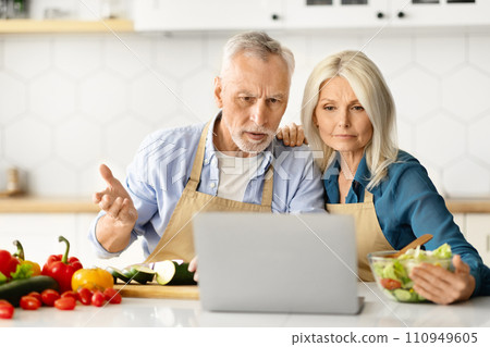 Wrong Recipe. Confused Senior Spouses Looking At Laptop While Cooking In Kitchen 110949605