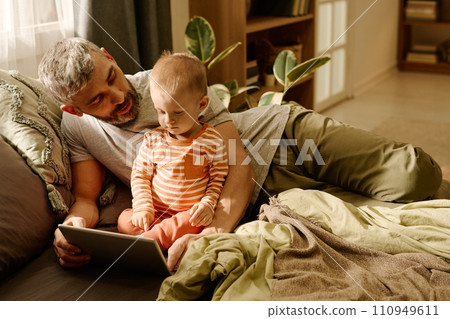 Man and baby boy relaxing on bed Man and baby boy relaxing on bed 110949611