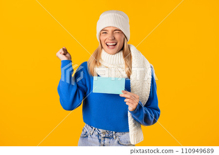 Joyful woman holding blank blue card, celebrating on yellow backdrop 110949689