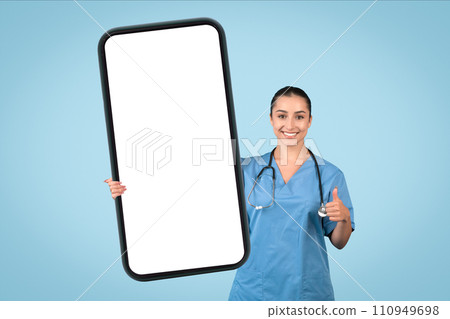 Happy female nurse with thumbs up holding a blank mobile phone 110949698