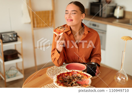 Woman savoring a slice of pizza in a cozy kitchen Woman savoring a slice of pizza in a cozy kitchen 110949710