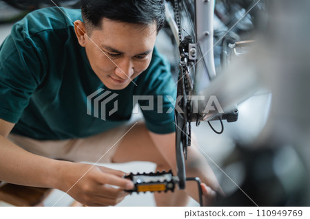 handsome young man repairing bicycle pedal with allens key in bicycle shop handsome young man repairing bicycle pedal with allens key in bicycle shop 110949769