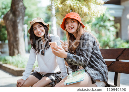 two Asian women in hats chatting about tourist destinations using mobile phones 110949898