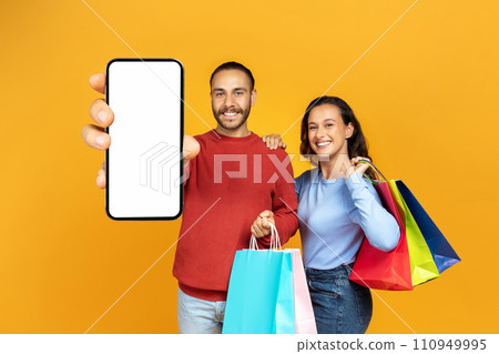 Cheerful millennial couple shopping online, showing smartphone 110949995
