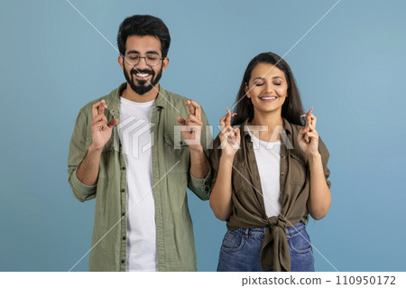 Excited millennial indian couple holding crossed fingers Excited millennial indian couple holding crossed fingers 110950172