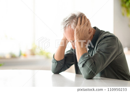 Portrait Of Depressed Senior Man Sitting At Table In Kitchen, Portrait Of Depressed Senior Man Sitting At Table In Kitchen, 110950233