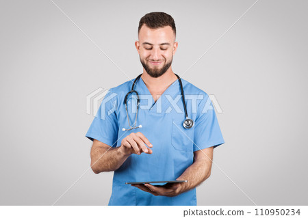 Doctor man in blue uniform using tablet and smiling on grey background Doctor man in blue uniform using tablet and smiling on grey background 110950234
