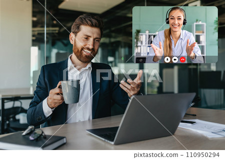 Handsome positive caucasian businessman talking with business partners via laptop Handsome positive caucasian businessman talking with business partners via laptop 110950294