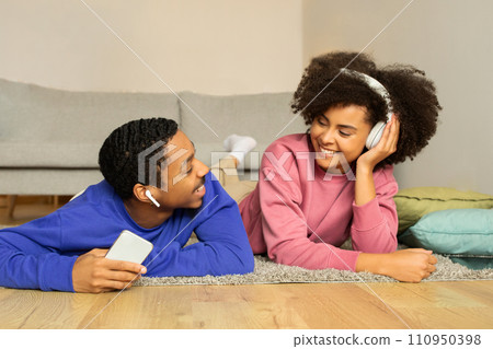 Black couple enjoys music online through headphones and cellphone indoor 110950398
