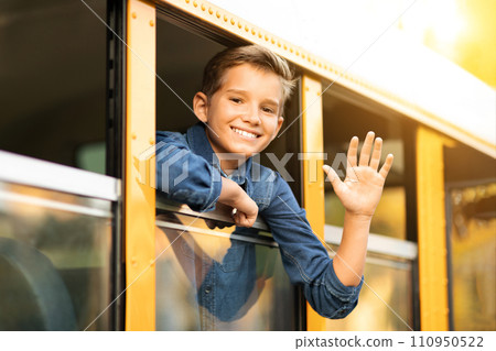 Happy preteen boy looking out of school bus window and waving hand Happy preteen boy looking out of school bus window and waving hand 110950522