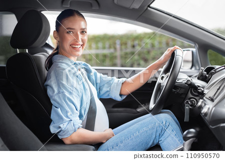 Cheerful pregnant woman sits confidently in driver's seat in automobile Cheerful pregnant woman sits confidently in driver's seat in automobile 110950570