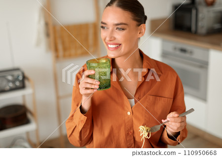 Smiling woman with a drink and spaghetti in modern kitchen 110950668