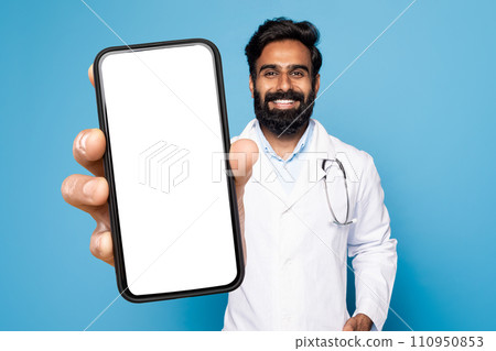Indian physician man in uniform demonstrating smartphone on blue background 110950853