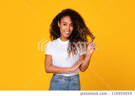 African American woman touching curly hair smiling over yellow background African American woman touching curly hair smiling over yellow background 110950859