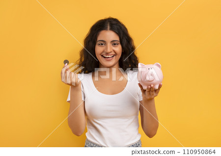 Emotional young woman with piggybank and coin on yellow Emotional young woman with piggybank and coin on yellow 110950864