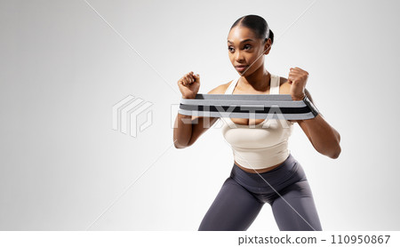 Black athletic lady exercising with rubber resistance band, white backdrop 110950867