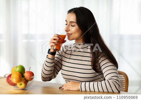 Glad young arab woman drink glass of fresh tasty juice in living room, kitchen interior 110950869
