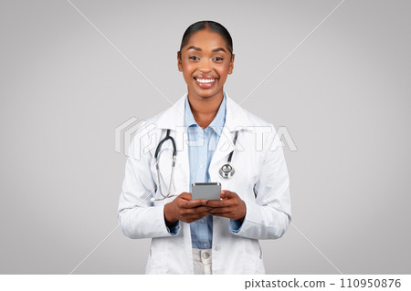 Positive millennial black lady doctor in white coat, typing on mobile phone, chatting on gadget Positive millennial black lady doctor in white coat, typing on mobile phone, chatting on gadget 110950876