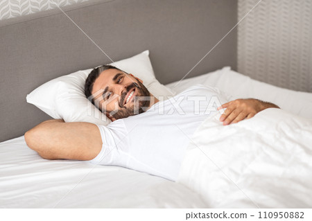 Relaxed European man happily lounging in comfortable bed in bedroom 110950882