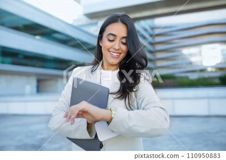 Latin entrepreneur woman smiling checking watch standing with laptop outdoor 110950883