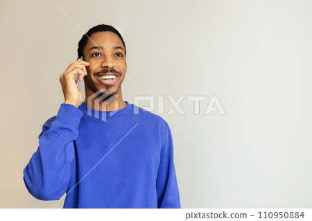 Black man engrossed in phone call standing against white wall 110950884
