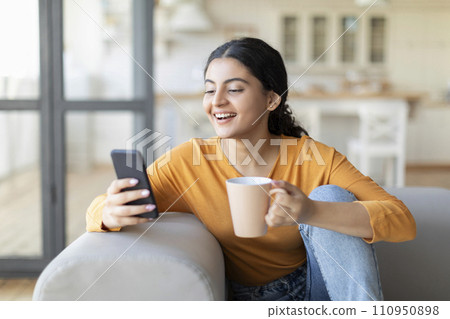 Weekend Leisure. Smiling Indian Woman Relaxing On Couch With Smartphone And Coffee 110950898