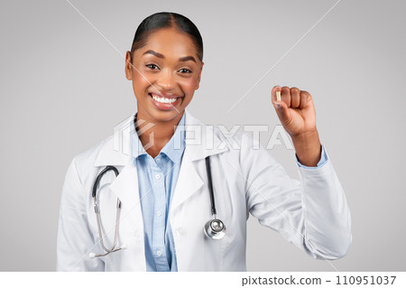 Happy millennial pretty black woman doctor show pill capsule, isolated on gray background 110951037