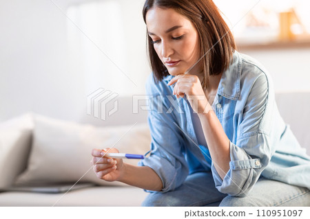 Unhappy young lady holds negative pregnancy test in living room Unhappy young lady holds negative pregnancy test in living room 110951097