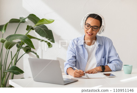 Smiling young latin lady in headphones work, study at table, has video call 110951146