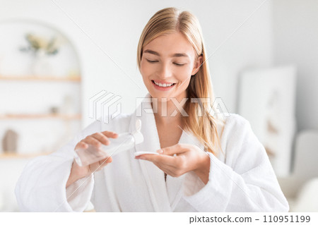 blonde woman applies micellar water on cotton pad in bathroom 110951199
