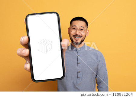 Asian man holding large smartphone with blank screen, yellow backdrop Asian man holding large smartphone with blank screen, yellow backdrop 110951204