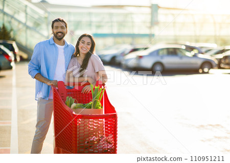 Cheerful arab couple with shopping cart outdoors, free space Cheerful arab couple with shopping cart outdoors, free space 110951211