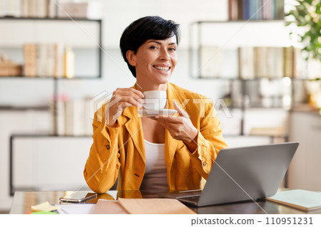 Contented middle aged business lady enjoying tea at workplace Contented middle aged business lady enjoying tea at workplace 110951231