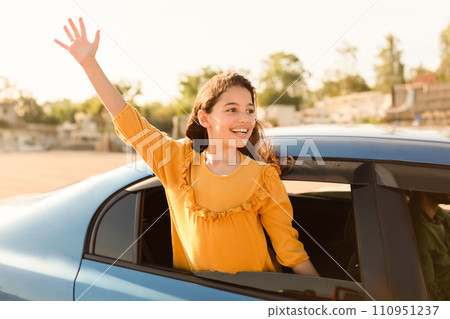 Happy girl waving from car, urban backdrop 110951237