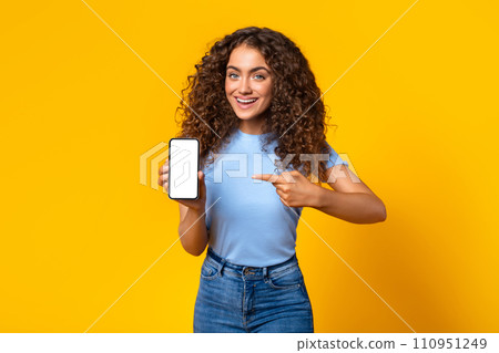Cheerful woman showing smartphone screen on yellow Cheerful woman showing smartphone screen on yellow 110951249