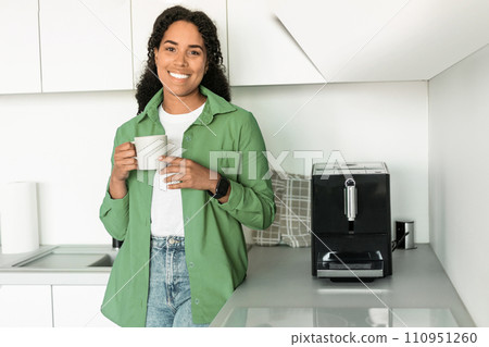 African American woman stands in her kitchen near coffee maker 110951260