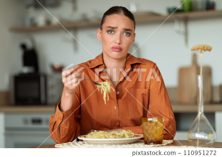 Doubtful upset woman tasting noodles in modern kitchen 110951272
