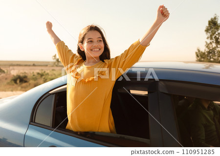 Joyful girl with arms raised from car, sunny day 110951285