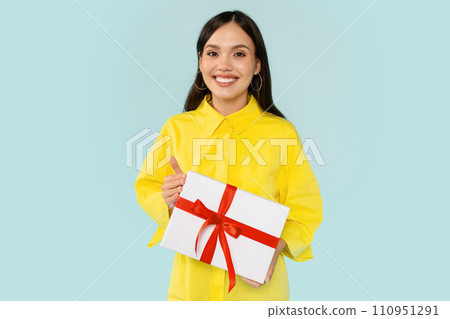 Positive young woman holding gift box and smiling Positive young woman holding gift box and smiling 110951291