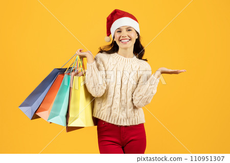 woman in Santa hat holds shopping bags against yellow backdrop 110951307