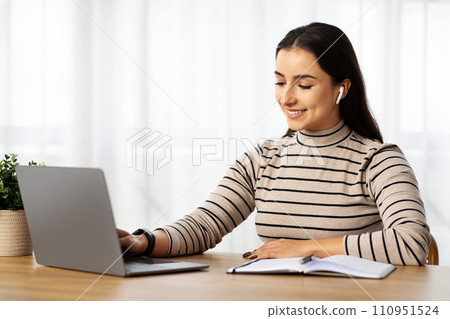 Positive young arab lady manager work at computer with wireless headphones, make notes Positive young arab lady manager work at computer with wireless headphones, make notes 110951524