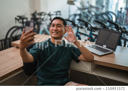 young man makes video call using cell phone while working at desk young man makes video call using cell phone while working at desk 110951572