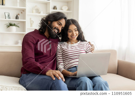 Loving cheerful indian couple using laptop together Loving cheerful indian couple using laptop together 110951605