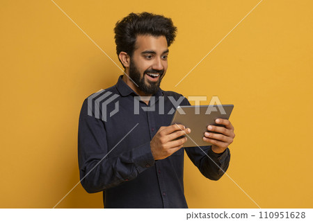 Happy young indian man playing online games on digital tablet Happy young indian man playing online games on digital tablet 110951628