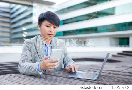 Korean business guy texts and browses laptop in city Korean business guy texts and browses laptop in city 110951680