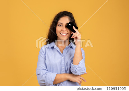 Positive latin millennial brunette lady in casual put credit card to eye, has fun, think at sale 110951905