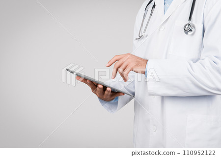 Doctor using a digital tablet, white coat, grey background, free space 110952122