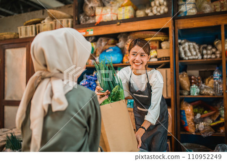 female greengrocery seller giving customer fresh vegetables female greengrocery seller giving customer fresh vegetables 110952249