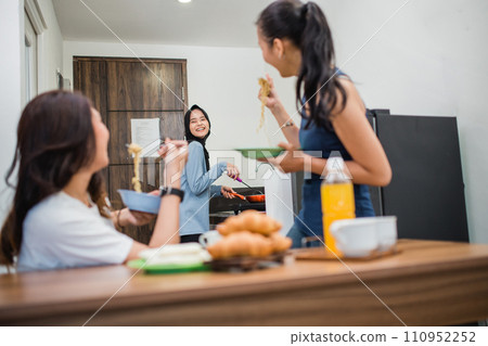 three Asian girls joke while making breakfast together in the kitchen three Asian girls joke while making breakfast together in the kitchen 110952252