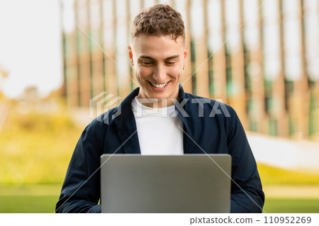 Smiling attractive young european guy in casual enjoy lifestyle, work on laptop in park on grass 110952269
